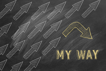 A unique yellow arrow breaks formation against a lot of white arrows on a chalkboard, highlighting the concept of going ones own way and individuality.