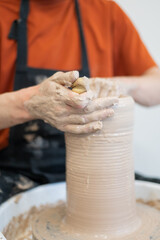Close-up of a potter's hands making a ceramic vase on a potter's wheel. Vertical photo. 