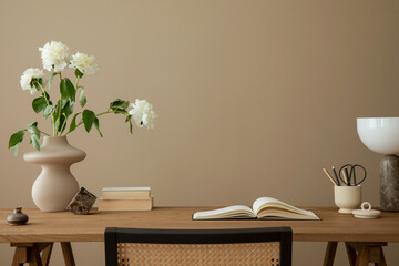 Warm and cozy workplace interior with wooden desk, rattan chair, vase with flowers, books, marble...