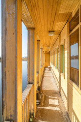 Sunny terrace of old wooden landing stage hotel on calm river in early morning. Empty path on guest...
