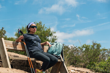 Hiker rests on a wooden bench located at the top of a mountain.