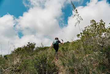 Hiker climbs the mountain surrounded by bushes with a nice blue sky with clouds.