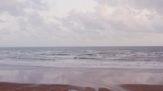 4K aerial view of sea waves on sandy beach with clouds in sky at Mandvi, Kutch, India. Calm coastline with sandy beach. Tropical vacation, beach holidays concept. Monsoon clouds at beach.