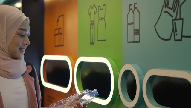Muslim woman puts a plastic water bottle in a waste bin for recycling.
