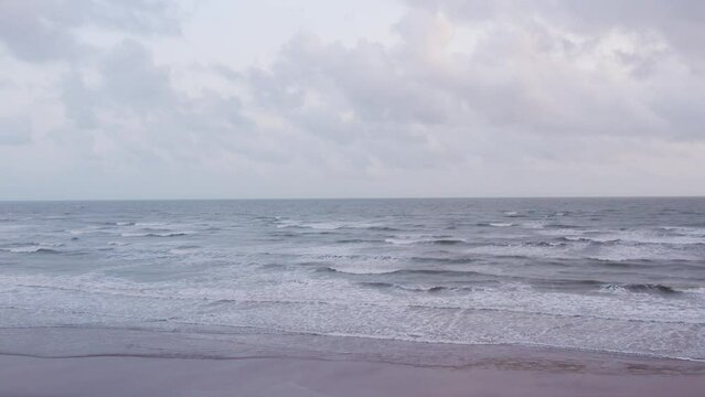 4K bird eye view of sea waves on sandy beach with clouds in sky at Mandvi, Kutch, India. Calm coastline with sandy beach. Tropical vacation, beach holidays concept. Monsoon clouds at beach.