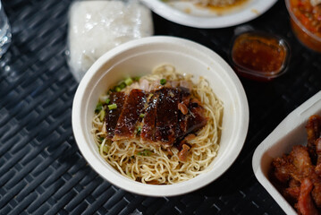 Roast duck noodles in a foam bowl on a black rattan table