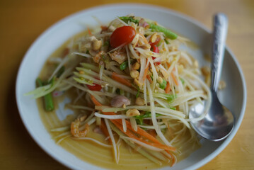 Thai papaya salad in a white plate and stainless steel spoon on the table