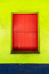 Red window on the facade of a green house. Vertical.