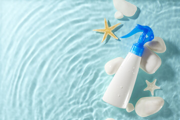 Sunscreen spray bottle on blue water background with starfish and white stones. Ideal for summer and skincare advertisements