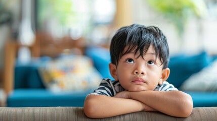 Young Indonesian boy sitting on a couch with arms crossed, lost in thought