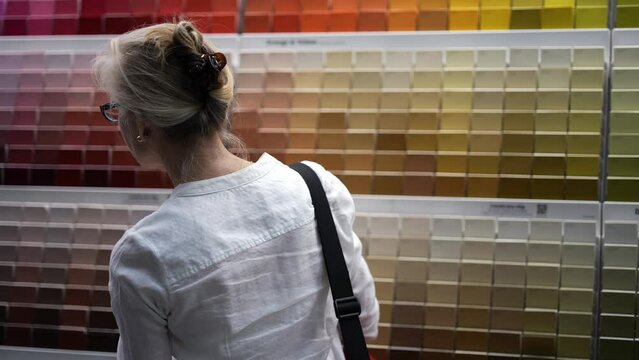 Back of blonde woman with large array of paint swatches in the background as she shops for good colors for home remodeling project.
