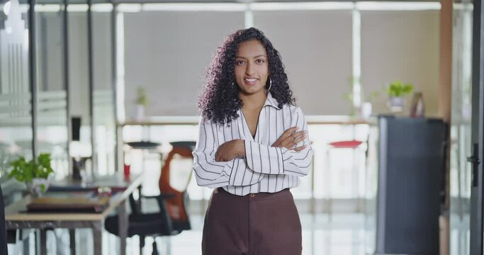 Indian Asian curly hair young adult gen z cute teen age expert girl cross arms standing proud look cam indoor office day happy woman lady staff agent fold hand do pose head shot video job work place