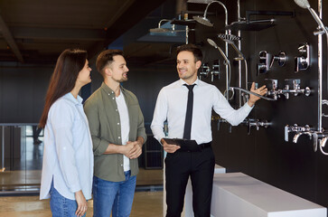 Young happy couple choosing sanitary taps and shower for their bathroom standing with male friendly...