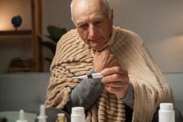 Close-up of man in blanket, holding thermometer with one hand. Treatment for coronavirus.