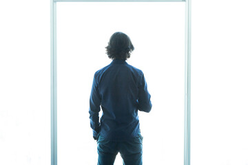 View of a young man with smartphone looking at a bright white blown out window in an office