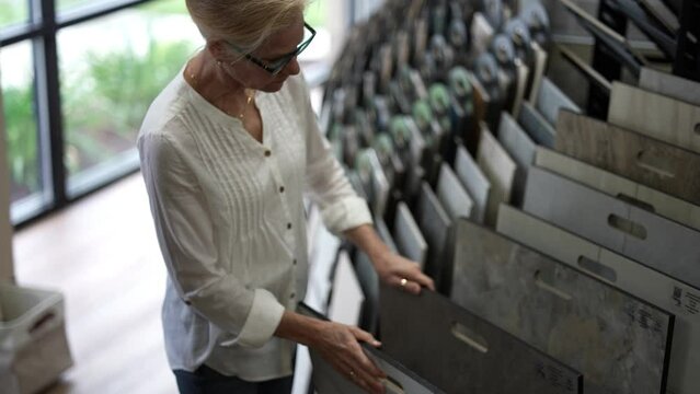 Happy mature woman touching sample flooring for home renovation redecorating project in a design center showroom.