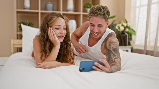 Smiling couple lounging on bed taking selfie with smartphone in a cozy bedroom