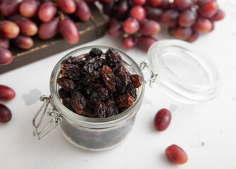 Dark dried sweet raisins in glass jar on light background.Macro