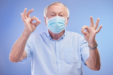 Elderly man, portrait and okay for face mask in studio, promote healthcare and prevention of virus. Male person, emoji and insurance for wellness on blue background, protocol and protect against flu