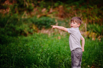 Young boy in a gray t-shirt and jeans, enthusiastically pointing at something in the distance while...
