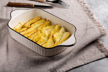 Zucchini wedges baked in oven in ceramic baking dish.