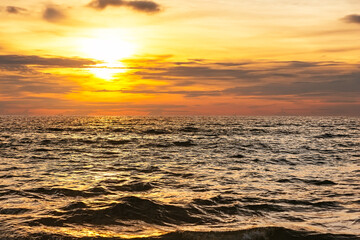 Amazing golden sunset with sea waves against a cloudy sky in Phuket, Thailand.