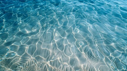 Obraz premium Crystal clear blue water with sunlight reflections creating mesmerizing patterns on the surface. Perfect for backgrounds and nature themes.