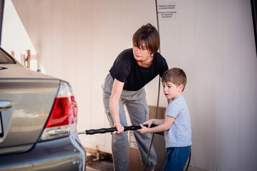 Mother closely assisting her young son as they wash the rear of a car at a self-service station....