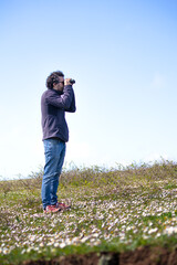 Curly haired young Turkish man watching nature with binoculars. Watcher person.	