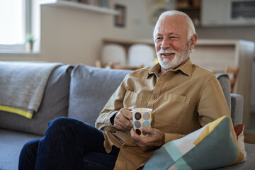 Vibrant senior Caucasian man relaxing at home. He is sitting on the sofa in his living room...