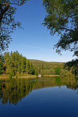 The view West over the Glen Ogil Reservoir one early morning over to the wooden Boathouse on the lake margins.