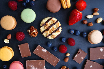 Macarons, chocolate, cookies, berries and various nuts on dark blue background. Top view.