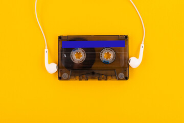 Wired headphones with audio tape on a yellow background. Retro style, DJ. Top view, minimalistic...