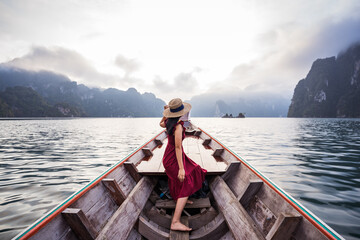 Asian female tourist on a long-tailed wooden boat in the morning, mountain and fog background.