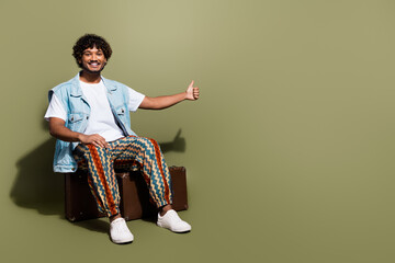 Full length photo of nice young male sit retro valise hitching car dressed stylish denim garment isolated on khaki color background