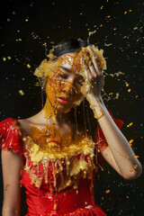 Woman in red dress covered in honey on black background.