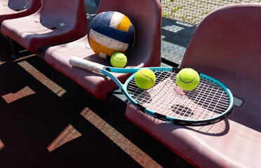 a tennis racket, balls and a volleyball on a bench on the sports tribune