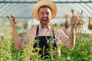 Cheerful facial expression. Man in greenhouse is working with plants