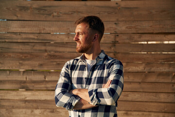 Man in checkered shirt is standing against wooden wall