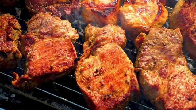 Meat Cooking on Grill. Pork Chunks grilling on grate close-up, sizzling and smoking. Juicy steak with grilling stripes preparing for picnic celebration