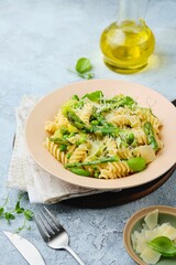 Pasta primavera, fusilli with green peas, asparagus and parmesan cheese in a ceramic plate on a gray concrete background. Asparagus recipes. Italian Cuisine.