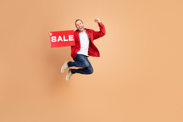 Full size photo of nice young man jump raise fist sale card wear red shirt isolated on beige color...