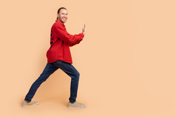 Full size profile photo of nice young man arms push empty space wear red shirt isolated on beige color background