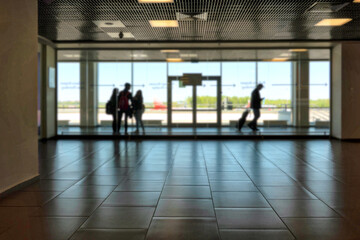 Fragment of the airport interior in backlight. Behind the glass wall, silhouettes of passengers and...