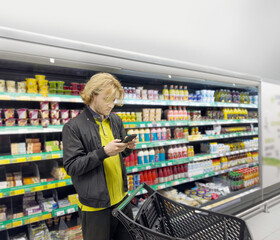 Shot of a young man shopping in a grocery store, using his smartphone to look up ingredients and prices wile choosing items at the supermarket.