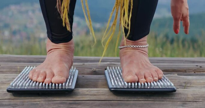 Yoga person standing on sadhu boards with sharp nails in mountains. Close up of female in sportswear, demonstrating pitted feet, after using sadhu boards in slow motion. Yoga equipment concept. 