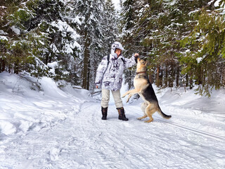 Adult girl or mature lady with shepherd dog in winter nature landscape in a forest. Middle aged woman training big shepherd dog in cold day. Friendship, love, communication, fun, hugs