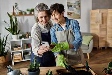 Two women in aprons photographing a lush potted plant together.