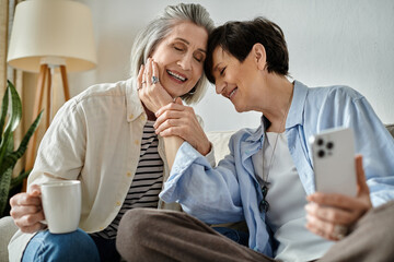 Two elderly women sitting on a couch and engrossed in their phones.