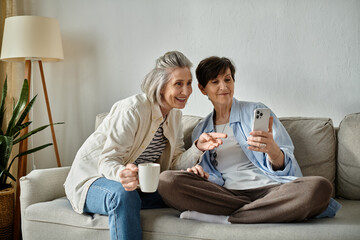 Two elderly women on a sofa mesmerized by their phones.